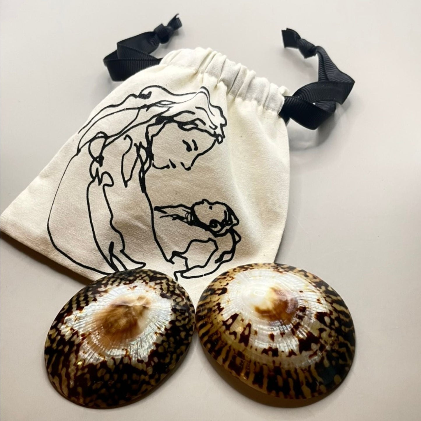 une pochette avec un dessin d'une maman qui regarde dson bébé dans les yeux et une paire de coquillages d'allaitement en nacre de chez bebe nacre